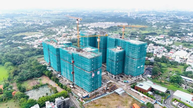 Aerial site photograph of Elysian in November 2025: four towers risen to their upper floors under green safety netting, with three tower cranes on site