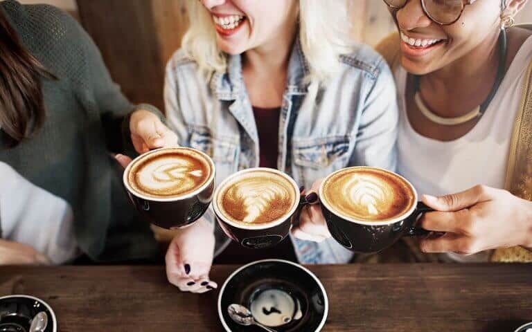 Three friends raising coffee cups together at a cafe table