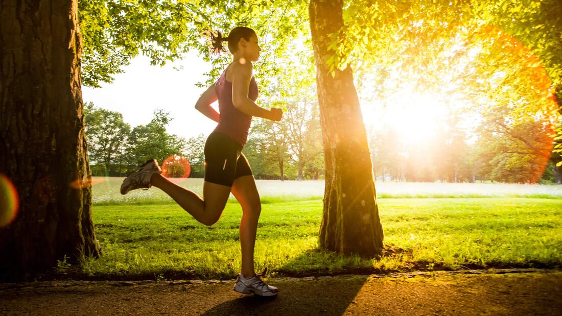 A woman running along a tree-lined path at sunrise